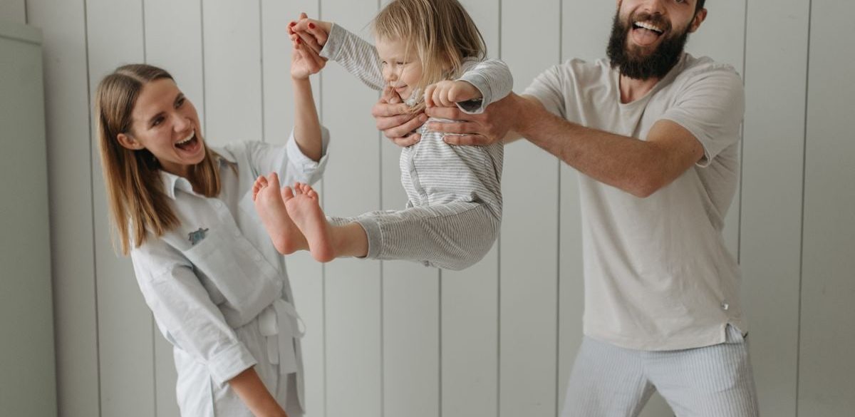 Joyful parents playing with their daughter indoors, all wearing white, capturing a moment of happiness.