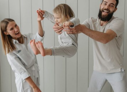Joyful parents playing with their daughter indoors, all wearing white, capturing a moment of happiness.