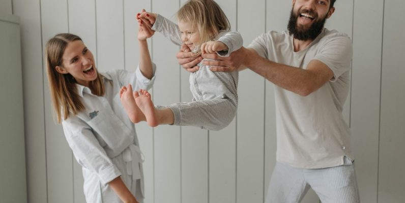 Joyful parents playing with their daughter indoors, all wearing white, capturing a moment of happiness.